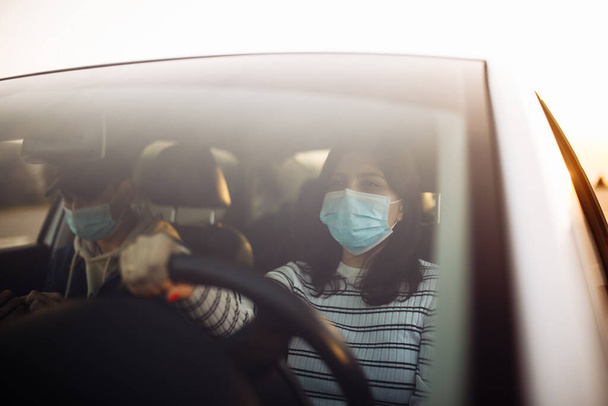 男の子と女の子の車の滅菌医療マスクを着用運転。市内のコロナウイルス隔離中に交通渋滞に巻き込まれた乗客を持つタクシー運転手。covid-19の概念の普及を防ぐ - 写真・画像