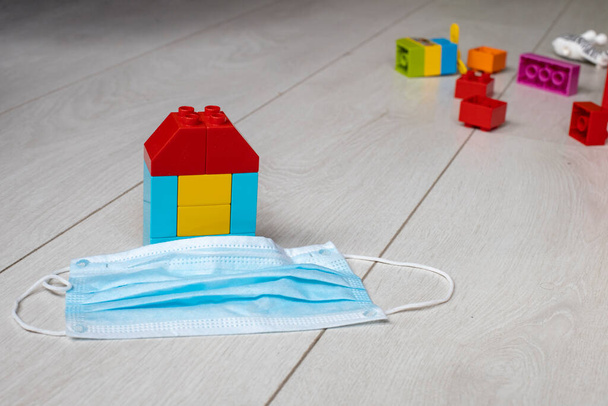концепція сімейної безпеки в пандемії коронавірусної хвороби -19. будинок дитячих блоків знаходиться на підлозі поруч з медичною маскою на барвистих іграшках
 - Фото, зображення
