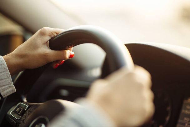 Zbliżenie dłoni kobiety na kierownicy, bezpiecznie odizolowanej podczas kwarantanny pandemii koronawirusowej. Ręce dziewczyny z czerwonymi gwoździami trzymającymi kierownicę i prowadzącymi samochód. Koncepcja transportu prywatnego - Zdjęcie, obraz