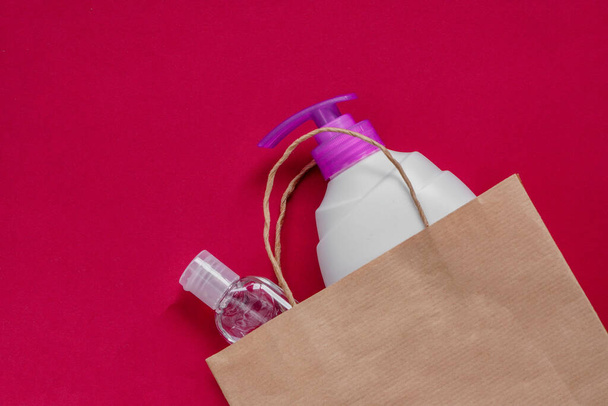 Paper bag with plastic bottles, liquid soap and gel sanitizer as protection for protection against coronavirus. Disinfectant, contactless delivery and personal hygiene.Flatlay on maroon, zero waste. - Photo, Image