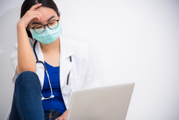 Азійська молода жінка-лікар носить маску до безпеки Коронавірус сидить на підлозі, дивлячись на ноутбук з сумом, стресом і хвилюючись про проблему, Концепція бережи себе, зупинити епідемію Ковід-19 - Фото, зображення