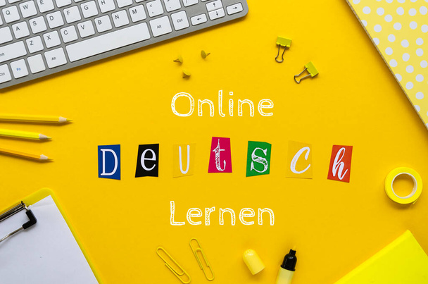 Firma en línea de DEUTSCH LERNEN en una mesa de estudiantes enmarcada con papelería de oficina y teclado para PC. Vista superior sobre fondo amarillo
 - Foto, Imagen