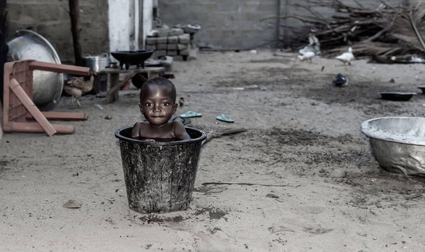 Африканский ребенок остывает в ведре с водой в жаркий день. Фото из рыбацкой деревни Ада Фоа Гана Западная Африка
. - Фото, изображение