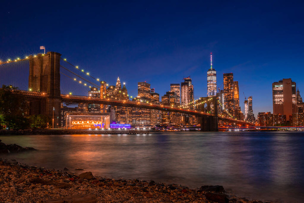 Волшебный вечерний вид на Бруклинский мост из Бруклинского парка с видом на нижний Манхэттен с другой стороны реки Гудзон. - Фото, изображение