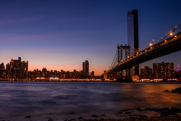Волшебный вечерний фиолетовый вид на Бруклинский мост с Бруклинского парка с видом на нижний Манхэттен с другой стороны реки Гудзон
. - Фото, изображение