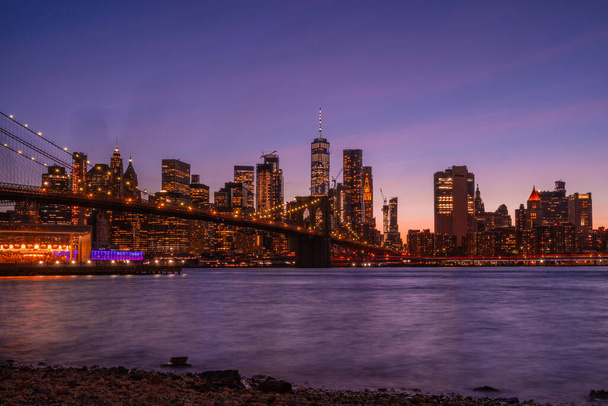 Волшебный вечерний фиолетовый вид на Бруклинский мост с Бруклинского парка с видом на нижний Манхэттен с другой стороны реки Гудзон
. - Фото, изображение