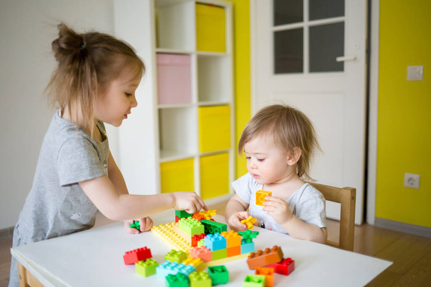kid play in the constructor. small child builds a castle out of blocks. concept of development of fine motor skills. joint games at home. sister teaches baby - Фото, изображение