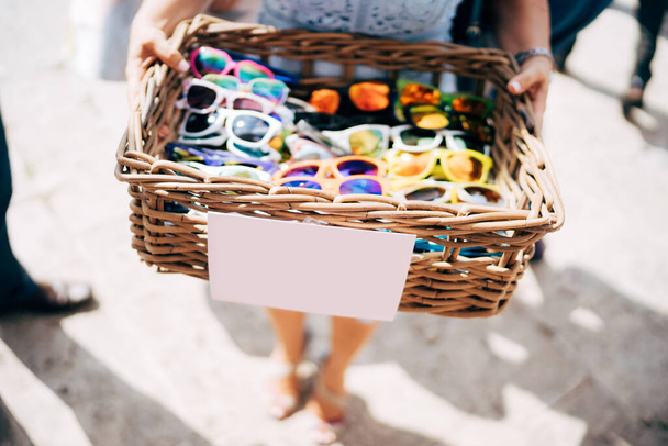 Un cesto di bicchieri. Un cesto di vimini di legno con occhiali da sole di diversi colori nelle mani di una ragazza
. - Foto, immagini