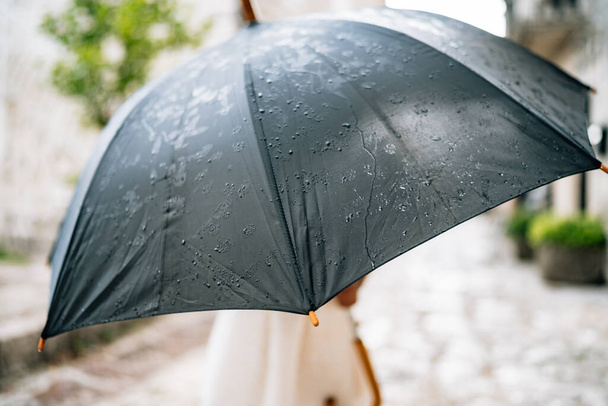 L'enfant pose avec un parapluie. Une petite fille en robe se tient dehors sous un parapluie noir sous la pluie
. - Photo, image