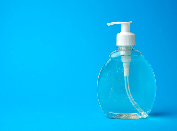 garrafa de plástico transparente com um desinfetante para desinfetar as mãos sobre um fundo azul, um lugar para inscrição
 - Foto, Imagem