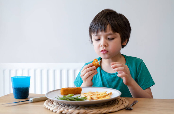 Retrato de un niño de 5 años con un dedo de pescado casero y papas fritas para la cena del domingo en casa, un niño feliz almorzando, niños comiendo comida heathy y fresca, concepto de estilo de vida saludable - Foto, Imagen