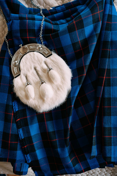 Pelo bianco sporran. Un marsupio SPORRAN, un capo d'abbigliamento nazionale scozzese decorativo, realizzato in pelliccia bianca con tre nappe. Sdraiato su un kilt a quadretti blu
. - Foto, immagini