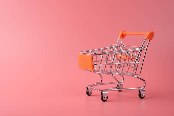 Photo of small silver shopping cart isolated over pink color pastel background with copy empty blank space - Fotó, kép