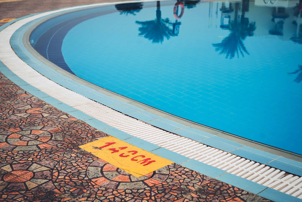 Temiz su ve derinlik göstergesi olan mavi yüzme havuzunu kapatın. Kızıl Deniz 'deki lüks otel, otel. Havuz suyundaki palmiye ağaçlarının ve binaların yansıması. Deniz kıyısındaki ilk otel..  - Fotoğraf, Görsel