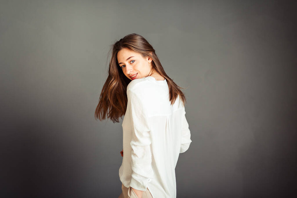 Fiatal lány fehér ingben, szürke háttérrel. Francia nő fehér blúzban, szürke falak mögött. Retusálás nélkül. - Fotó, kép