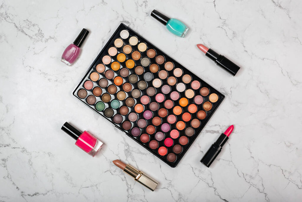 Flat lay of cosmetics products with colorful eyeshadow makeup palette on marble texture - 写真・画像