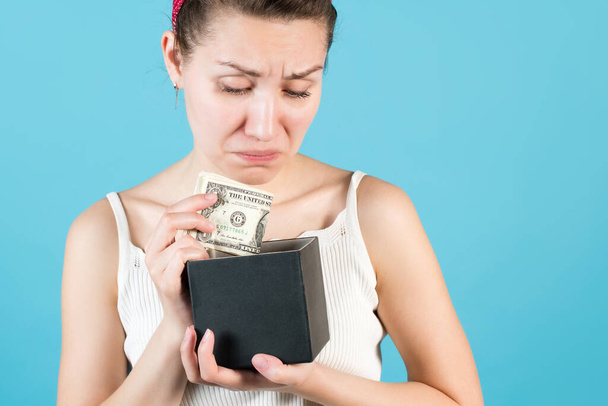 Close-up of a girl who puts or takes dollars out of a piggy bank box. Isolated on blue background. - Foto, imagen