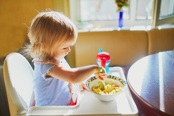 Adorable little girl eating pasta at home. Toddler enjoying her food. Healthy diet for small kids - Fotografie, Obrázek