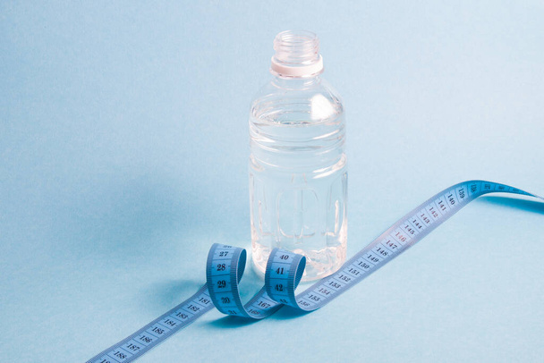 small bottle of water and a measuring tape on a blue background copy space, weight loss and healthy life social - Fotografie, Obrázek