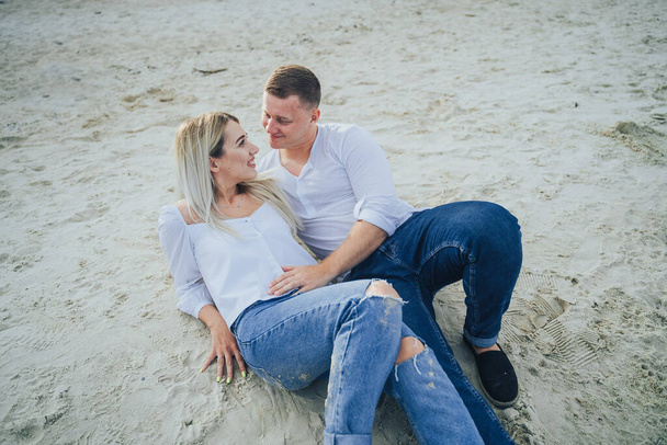 Hermosa pareja feliz en el amor acostado en una playa en la arena en una camisa blanca están en el amor sonriendo. Verano, vacaciones, vacaciones y gente feliz concepto
  - Foto, imagen