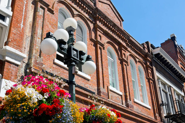 Bâtiment en brique en arrière-plan, bouquet de fleurs accroché à un lampadaire dans un vieux quartier du centre-ville
.  - Photo, image
