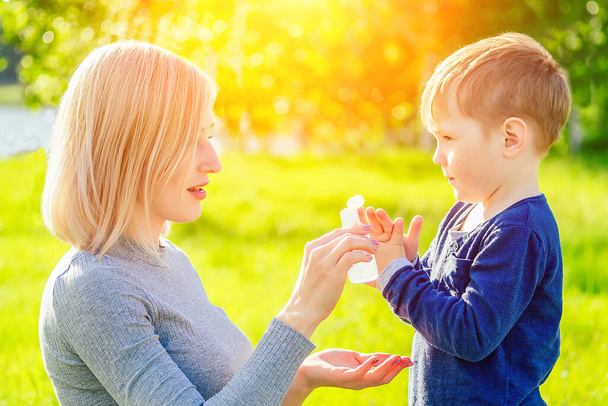 beautiful mother wipes her sons hands with wet hygienic napkins antibacterian sanitizer gel in the park in summer . anti bacterial napkins and freshness concept - Zdjęcie, obraz