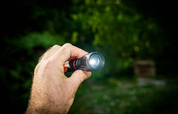 Hand-Test hält neue Mini-Taschenlampe grün defokussiert im Freien - Foto, Bild