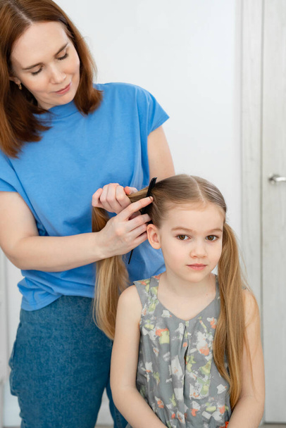 mom makes ponytails of her little daughter - Фото, изображение