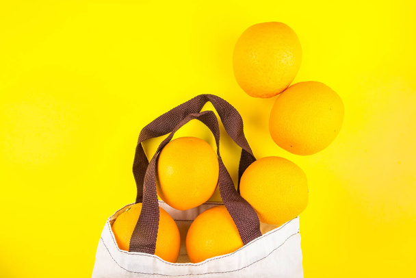 Сочные оранжевые апельсины в тканевом пакете, изолированном на желтом фоне.
. - Фото, изображение