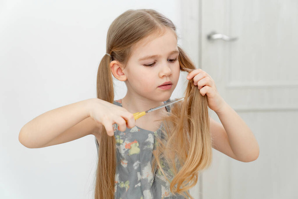 Egy kislány ollóval vágja a haját. - Fotó, kép