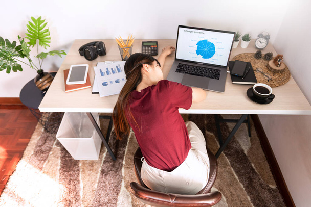 Vonzó fiatal gyönyörű ázsiai nő dolgozik laptop és dokumentum, miközben ül a beltéri nappali iroda, mint egy szabadúszó, e-coaching munka, távolról, vagy a munka otthonról koncepció - Fotó, kép