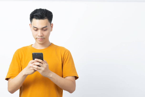 Jeune homme asiatique heureux lecture message de smartphone avec copyspace sur fond blanc
. - Photo, image