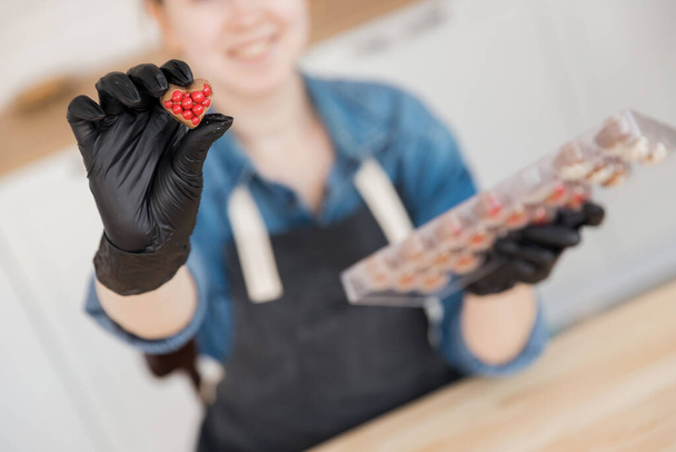 Confectioner holds sweet Belgian chocolate candies on kitchen background. Small business home concept - Photo, Image