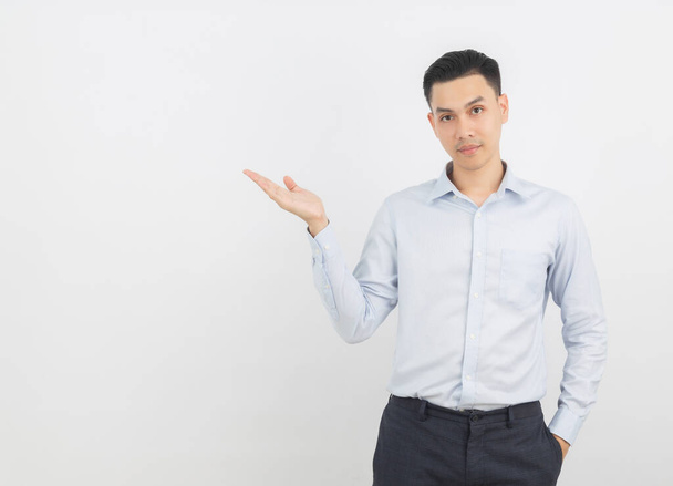 Fiatal ázsiai üzletember kék ing mutat oldalra egy kézzel, hogy mutasson be egy termék vagy egy ötlet, miközben keres a kamera elszigetelt fehér háttér. - Fotó, kép