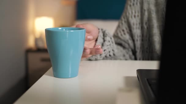 A női kéz vesz egy csésze kávét vagy teát az asztalról, majd visszateszi. A nő az asztalnál ül, laptopozik és forró italokat iszik. Otthoni munka, szabadúszó koncepció - Felvétel, videó