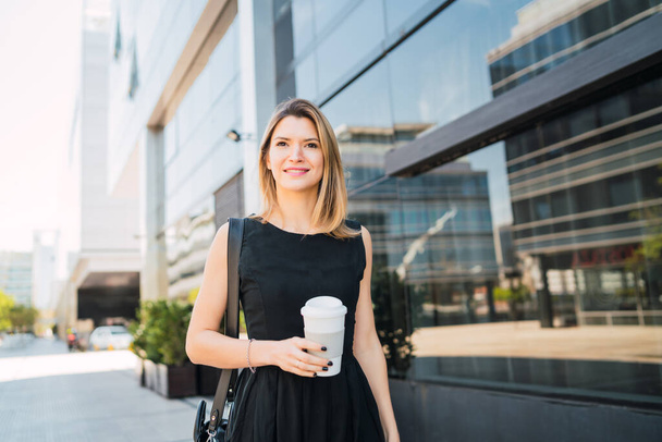 Portrait of young business woman walking to work while drinking takeaway coffee. Business and success concept. - Фото, зображення