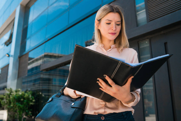 Portrait of young business woman holding clipboard while standing outdoors at the street. Business concept. - Foto, afbeelding