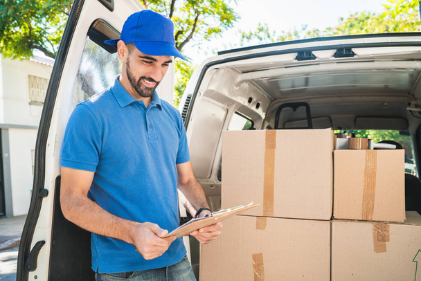 Portrait of a delivery man checking the products in checklist while standing right next to his van. Delivery and shipping concept. - Foto, imagen