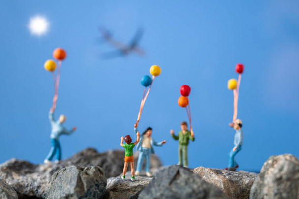Personas en miniatura, familia feliz sosteniendo globo en la roca con el fondo azul del cielo
 - Foto, imagen