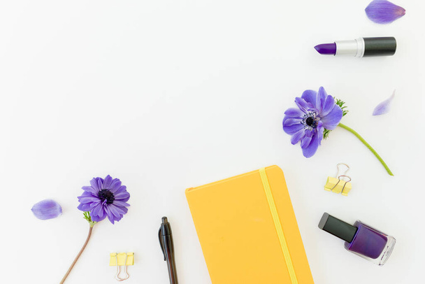 Frühlingskomposition mit gelbem Notizbuch, blauen Anemonen und Nagellack auf weißem Hintergrund. Flache Lage. - Foto, Bild