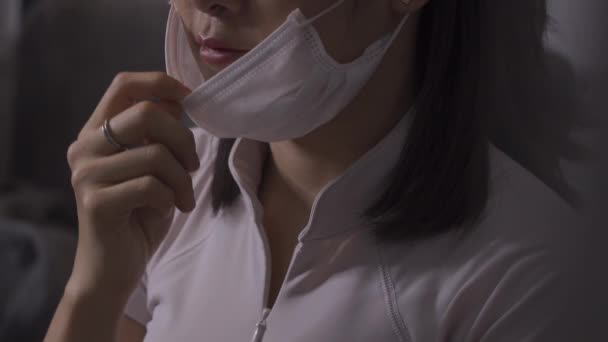 4k mladá asijská žena dávat na bílou masku, sedět na pohovce, bílá košile top, nemoc šíření, lékařské pojetí, bakteriální klíčky, lehká kůže model, Asie, vyléčit vakcíny - Záběry, video