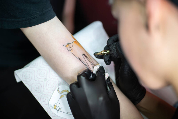 Tattoo artist making tattoo on female client's arm with tattoo machine - Foto, Imagem