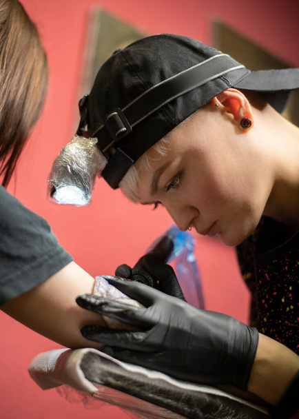Tattoo artist making tattoo on female client's arm with tattoo machine - Fotoğraf, Görsel