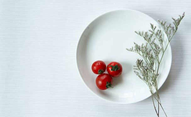 Tuoreet punaiset tomaatit ja kuivattu kukka valkoinen ruokalaji eristetty valkoinen ja harmaa viiva tausta
. - Valokuva, kuva