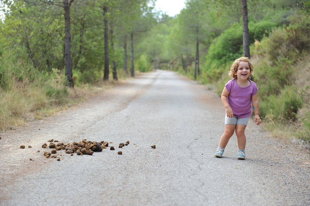 αστείο μικρό παιδί στο δρόμο έκπληκτος και γελώντας με περιττώματα αλόγων - Φωτογραφία, εικόνα