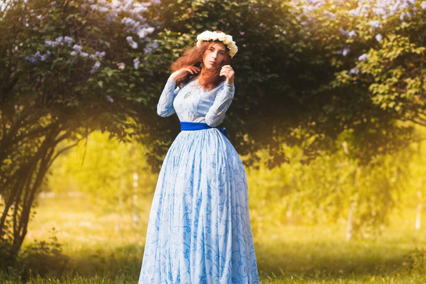 Привлекательная женщина в синем великолепном платье гуляет по парку на фоне цветущих лиловых цветов
. - Фото, изображение