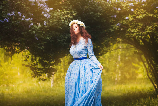Aantrekkelijke vrouw in een blauwe prachtige jurk wandelingen in het park tegen de achtergrond van bloeiende lila bloemen. - Foto, afbeelding