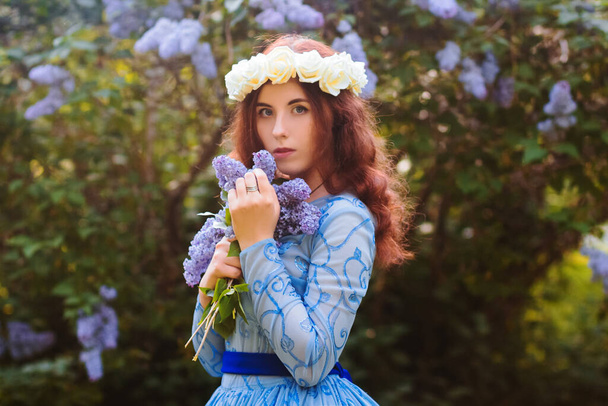 Привлекательная женщина в синем великолепном платье гуляет по парку на фоне цветущих лиловых цветов
. - Фото, изображение