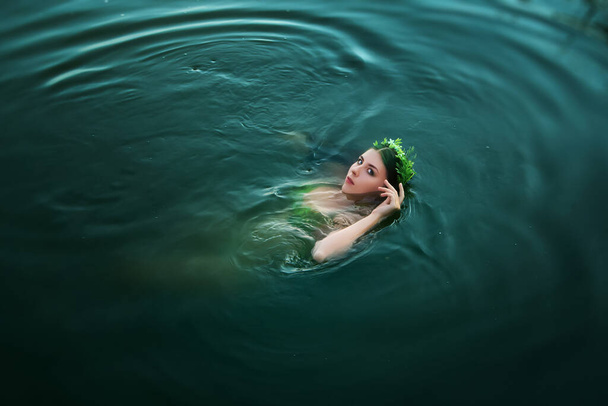 Красивая девушка в купальнике из зеленых растений с венком на голове плавает на спине в беспокойной воде. Концепция искусства хозяйки озера из легенд
. - Фото, изображение