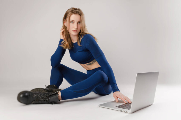 αθλητική κοπέλα που ποζάρει στο Studio εκτελεί ασκήσεις online σε ένα φορητό υπολογιστή σε λευκό φόντο - Φωτογραφία, εικόνα
